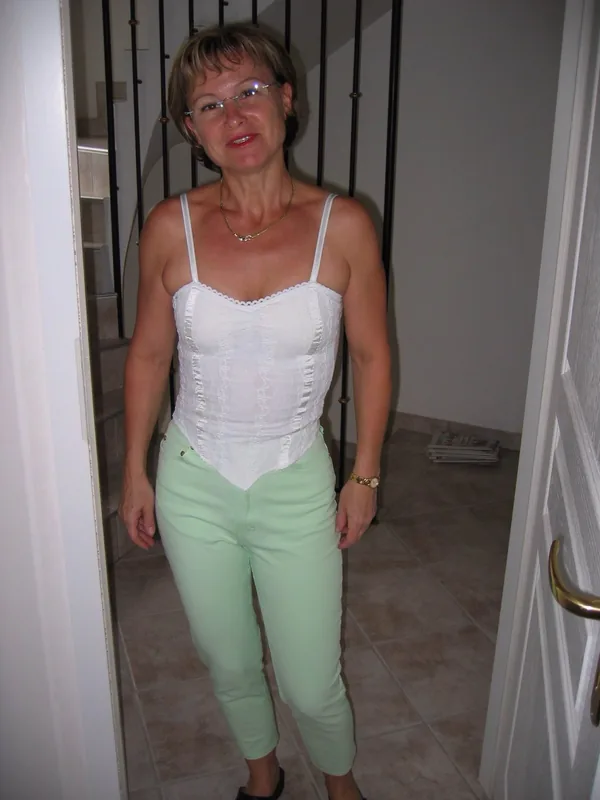 Personne en haut blanc à bretelles et pantalon vert pâle, lunettes, dans un couloir intérieur