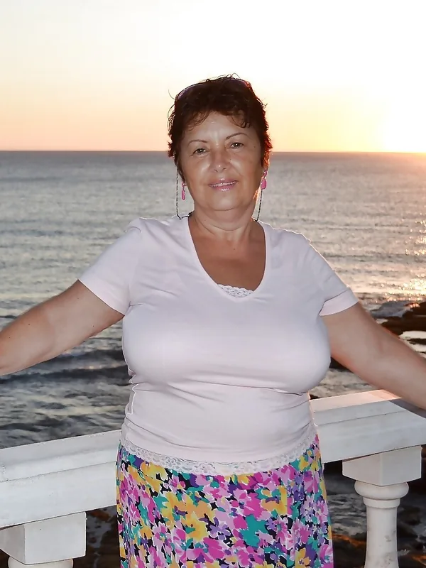 Personne en tenue colorée posant sur une balustrade face à la mer au coucher du soleil
