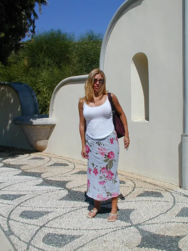 Femme blonde en tenue d'été posant devant un mur blanc avec un sol décoratif en galets.